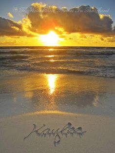 the sun is setting over the ocean with writing in the sand and clouds above it