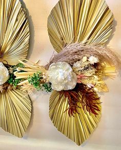 two gold fan shaped wall hangings decorated with flowers and foliage, each holding an artificial flower