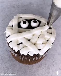 a cupcake decorated with white icing and black eyes is being piped into it