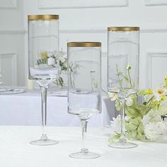 three clear wine glasses sitting on top of a table next to vases filled with flowers