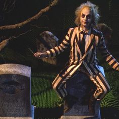 a creepy clown dressed in striped clothing walking through the dark grass with his hands out