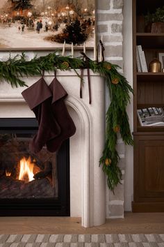 stockings hanging from a fireplace mantle decorated with greenery and pine cones, next to an open fire