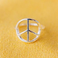 a silver peace sign ring sitting on top of a yellow blanket with the word peace written in it