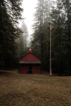 a small red building with an american flag on it's pole in front of some trees