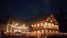 people standing on the porch of a house with christmas lights strung around it at night