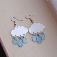 two white clouds with blue tears hang from silver earwires on a table