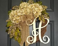 a wreath with the letter h on it hanging from a front door, decorated with flowers and leaves