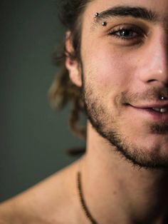 a man with piercings on his nose and chest smiling at the camera while wearing a chain around his neck