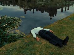 a man laying on the ground in front of a body of water with lily pads