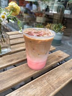 a drink sitting on top of a wooden table next to a vase filled with flowers