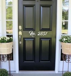 a black front door with two planters on either side and welcome mat in front