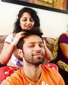 a man sitting on top of a couch next to a woman who is combing her hair