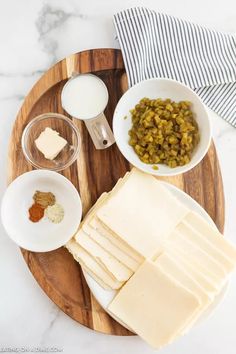 a wooden plate topped with lots of cheese and crackers next to bowls of food