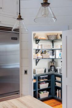 an open pantry in the middle of a kitchen with stainless steel refrigerator and wooden table