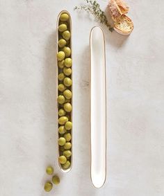 two metal containers filled with olives next to an empty spoon and flower on a white surface