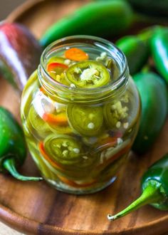 pickles and peppers in a glass jar on a wooden platter with green peppers