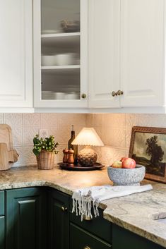 a kitchen with green cabinets and marble counter tops, including a bowl of fruit on the island