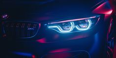 the front lights of a bmw car are illuminated in red and blue light at night