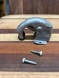 a piece of metal sitting on top of a wooden table next to two screws