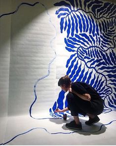 a man kneeling down in front of a blue and white wall with an artistic painting on it