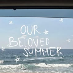 the words our beloved summer written in white chalk on a window sill at an ocean beach