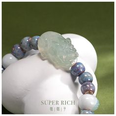 Discover the essence of prosperity with our Handmade Jadeite Pixiu Bracelet 天然翡翠貔貅. Each Pixiu charm is meticulously hand-carved from certified Grade A Jadeite, symbolizing wealth and positive energy in Feng Shui. This elegant bracelet features an adjustable elastic cord adorned with beautiful handmade ceramic beads, offering a unique blend of traditional craftsmanship and modern style. Ideal as a precious gift for a loved one or a protective talisman for yourself, this bracelet is more than jus Elegant Good Luck Bracelets With Natural Stones, Agate Bracelet With 108 Beads, Good Luck Jewelry With Round Natural Stone Beads, Elegant Handmade Crystal Bracelet For Meditation, Spiritual Jade Crystal Bracelet With Round Beads, Symbolic Hand-strung Round Beaded Bracelets, Elegant Turquoise Beaded Bracelets For Meditation, Handmade Jade Beaded Bracelets For Healing, Unique Jade Bracelets As A Gift