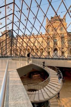 the inside of a glass building with stairs and people walking around in front of it