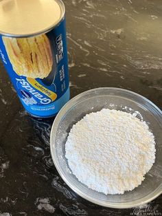 a can of soda and a bowl of flour on a table with a black counter top