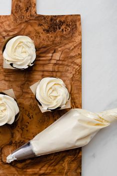 three cupcakes with white frosting sitting on a cutting board next to a knife