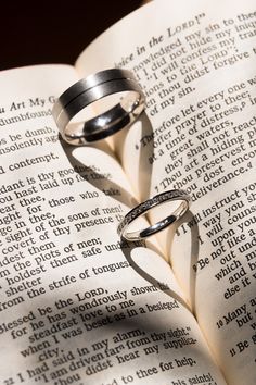 two wedding rings sitting on top of an open book with the word love written in it