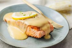 a piece of salmon covered in gravy on a blue plate with a fork