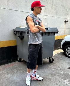 a man with his arms crossed standing next to a trash can