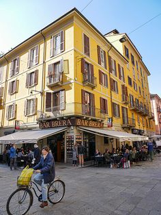 a man riding a bike down the middle of a street next to a tall yellow building