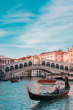 two gondolas on the water in front of a bridge with people riding them