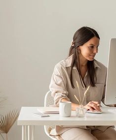 a woman sitting at a desk with a computer on her lap and coffee mug in front of her