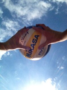 a person holding a beach ball in their hand under a blue sky with white clouds