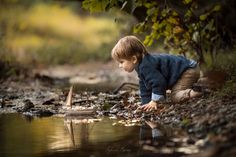 a young boy playing with a toy boat on the water's edge in a wooded area