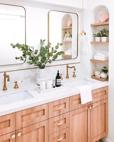 a bathroom vanity with two sinks, mirrors and plants on the countertop in front of it