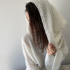 a woman in a white knitted hoodie sitting on a bed with her hands under her face