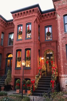 a large red brick building with wreaths and lights on the front door is decorated for christmas