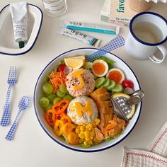 a bowl filled with meat, vegetables and fruit next to a cup of coffee on a table