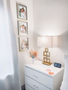 a white dresser with pictures on the wall above it and a lamp next to it