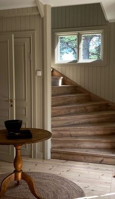 a table with a bowl on top of it in front of a stair case next to a window