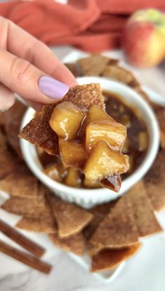 a person dipping some kind of food into a small white bowl filled with sauce on top of tortilla chips