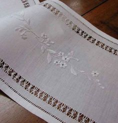 an embroidered tablecloth with white flowers and leaves on the edge is laying on a wooden floor