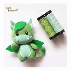 a green stuffed dragon next to a spool of thread