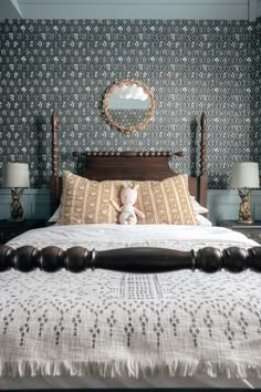 a teddy bear sitting on top of a bed in a room with blue walls and patterned wallpaper