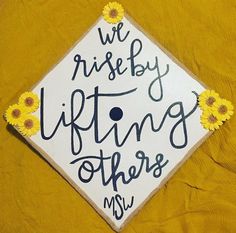 a graduation cap that says we rise by lifting others up with daisies on it