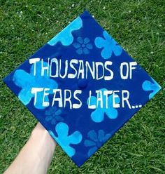 a blue graduation cap that says thousands of tears later on the grass with paw prints