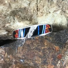 This beautiful Sterling Silver Ring, as part of the Red Moon Collection, features Black Jade, Kingman Turquoise and Blue, Green & Red Lab Opal. with a cascade of three small Cubic Zirconia in the center. Ring Width: 5/16" The ring is designed by David Rosales, one of the finest contemporary Southwest Artists in the world. He is the founder and co-owner of Supersmiths, Inc. of Gallup, NM. Each ring is custom made and carries a lifetime guarantee. Multicolor Fusion Jewelry With Accent Stones, Red Multi-stone Diamond Jewelry, Multicolor Fusion Style Jewelry With Accent Stones, Fine Jewelry With Inlay For Anniversary, Multicolor Multi-stone Opal Ring, Fine Jewelry Ring With Inlay As A Gift, Fine Jewelry Ring With Inlay For Gift, Fine Jewelry Ring With Inlay Perfect As A Gift, Fine Jewelry With Inlay As A Gift